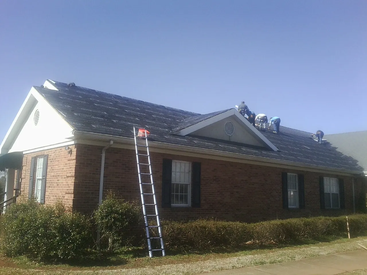 Crew tearing shingles off a brick ranch roof with a ladder set — Metal Roof Repair work by our crew in Plains