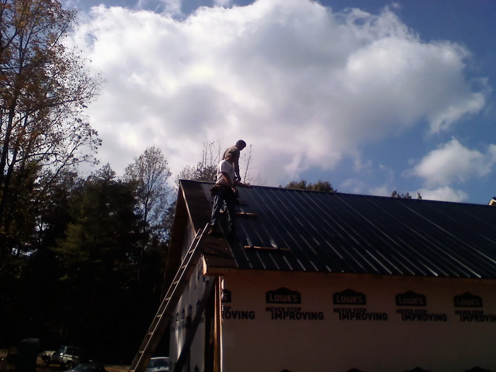 Roofer fastening dark metal panels high against a cloudy sky in Plains